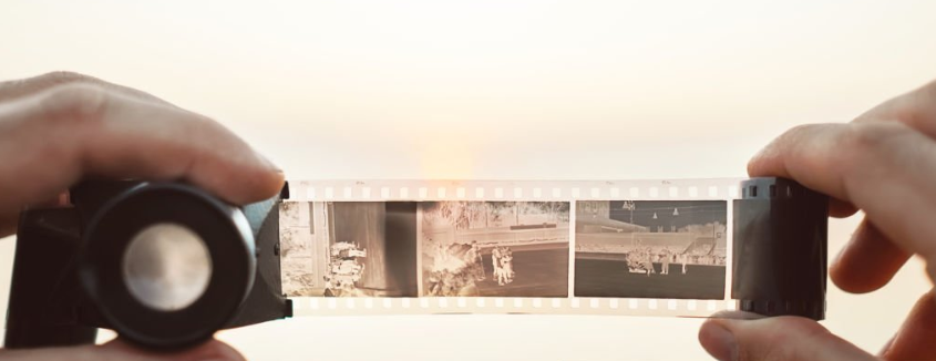 A strip of film held between two hands, with a lens on the left over the film